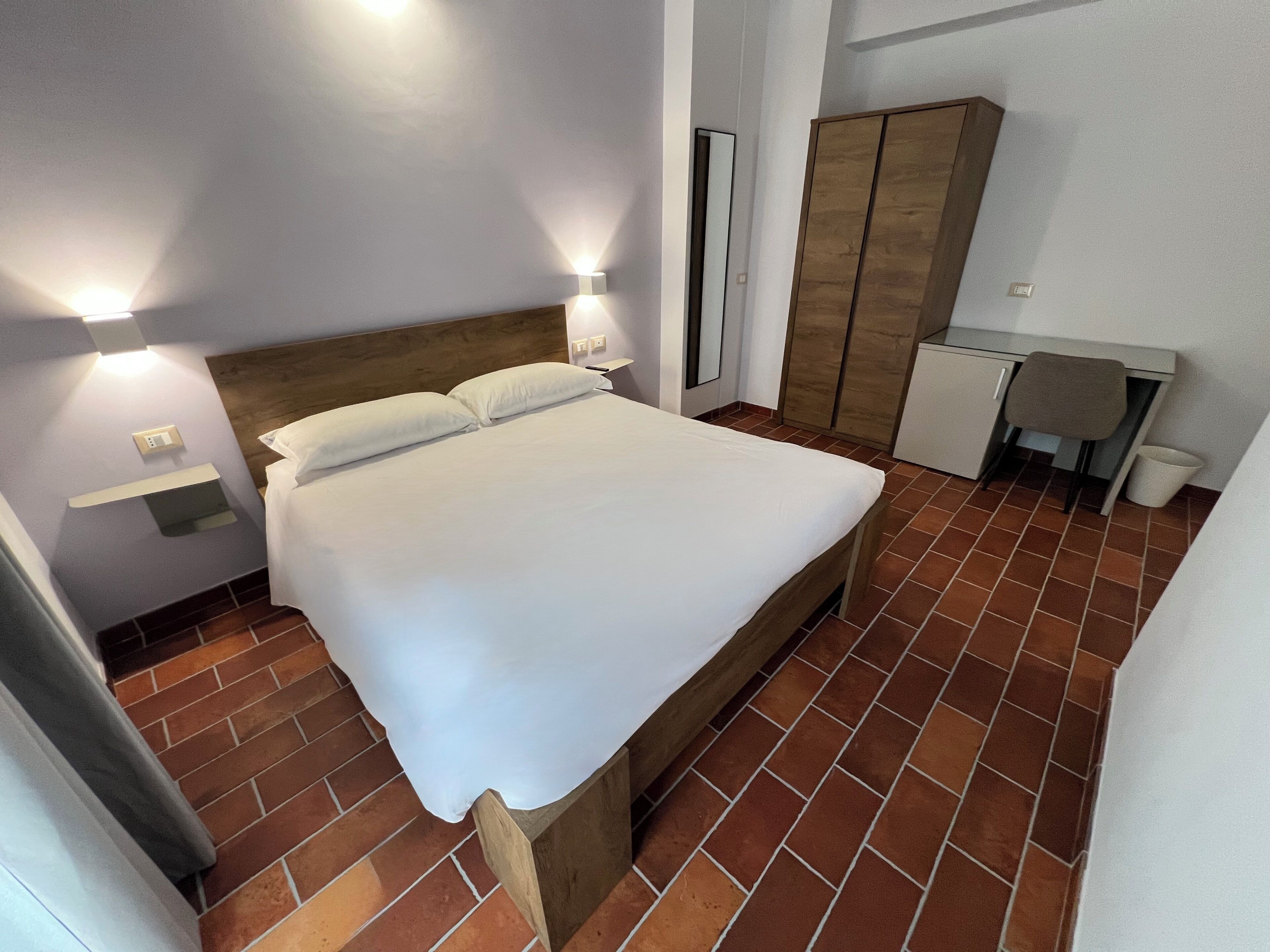 Un dormitorio con cama, lámparas de noche, armario y escritorio.