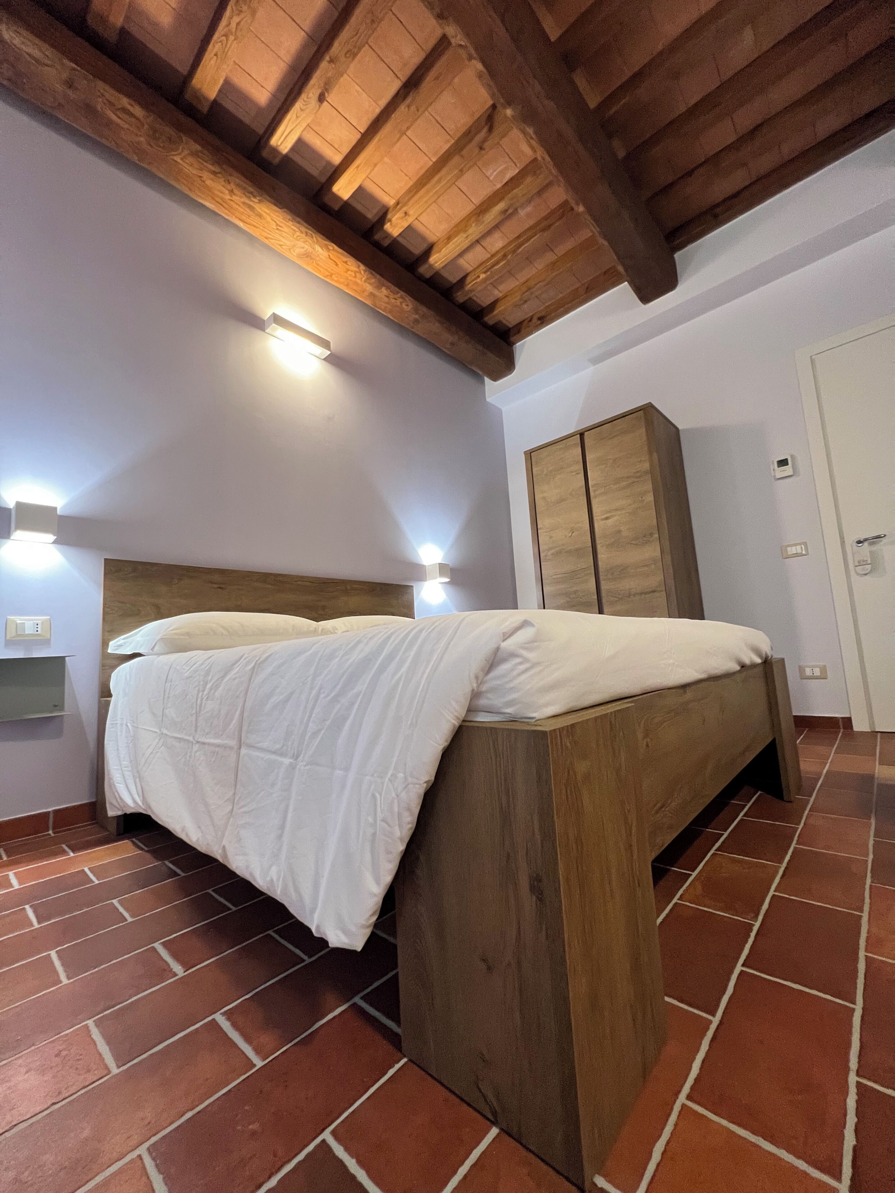A bedroom with a wooden bed frame, a wardrobe, and a tiled floor.