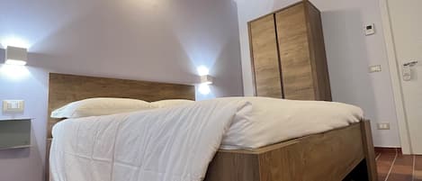 A bedroom with a wooden bed frame, a wardrobe, and a tiled floor.