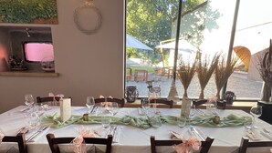 A dining area with a table set for four, chairs, a wall-mounted light, and a view through a large window.