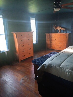 Une chambre à coucher avec une commode en bois, un lit recouvert d’une couvre-lit à motifs et une fenêtre avec des rideaux.