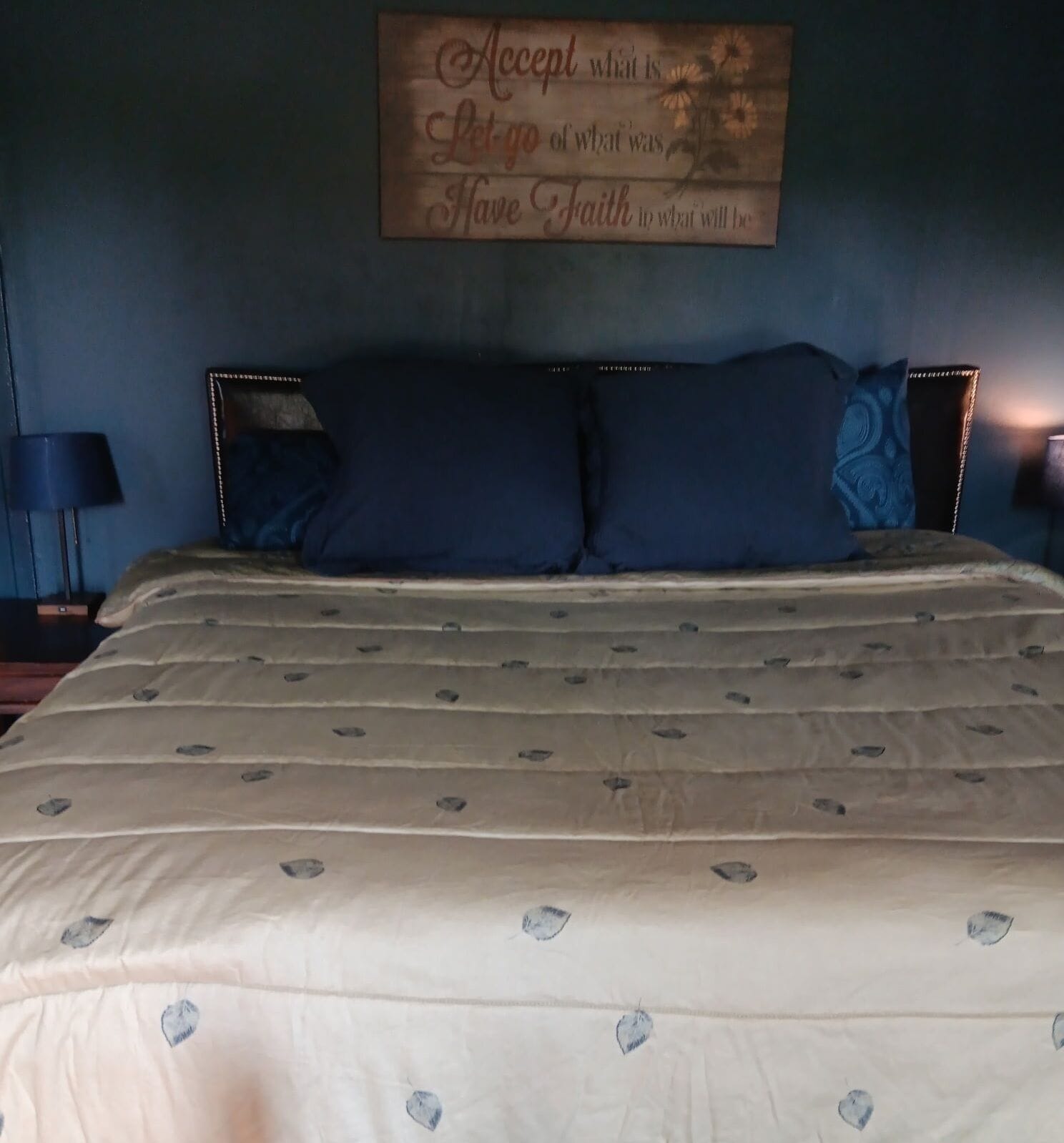 A bedroom with a bed, a wall-mounted sign, and a nightstand with a lamp.