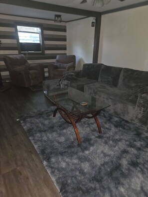 A living room with a glass coffee table, two sofas, and a striped wall. - Charming 3-bedroom house in Ava, NY. (Ava)