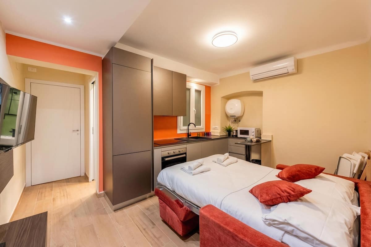 A hotel room with a bed, a TV, a kitchenette, and a bathroom.