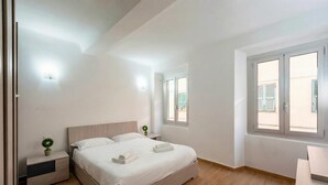 Ein Schlafzimmer mit einem Bett, Nachttischen, einer kleinen Pflanze und einem Fenster.