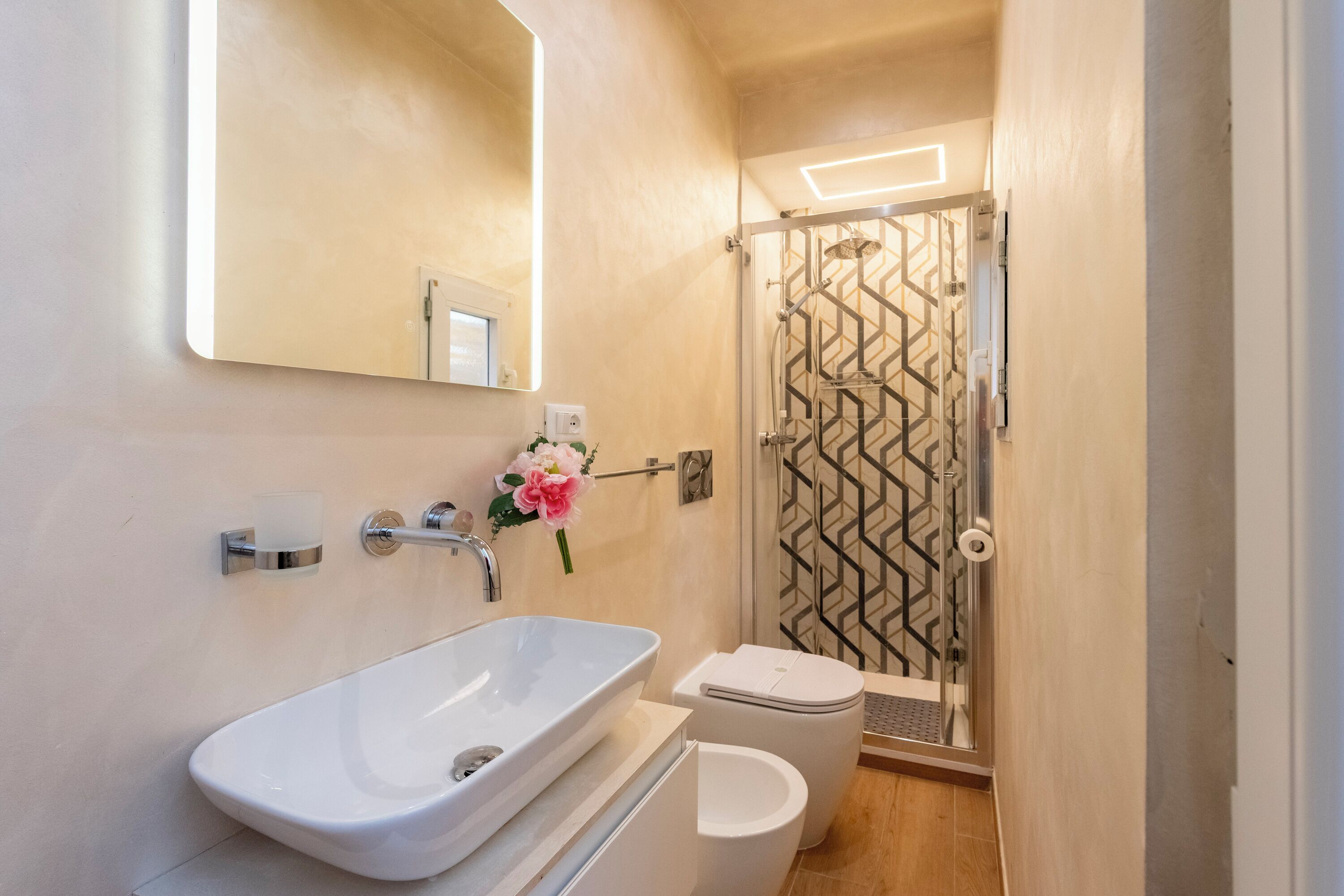 A bathroom with a white sink, a toilet, and a shower with a geometric glass door.