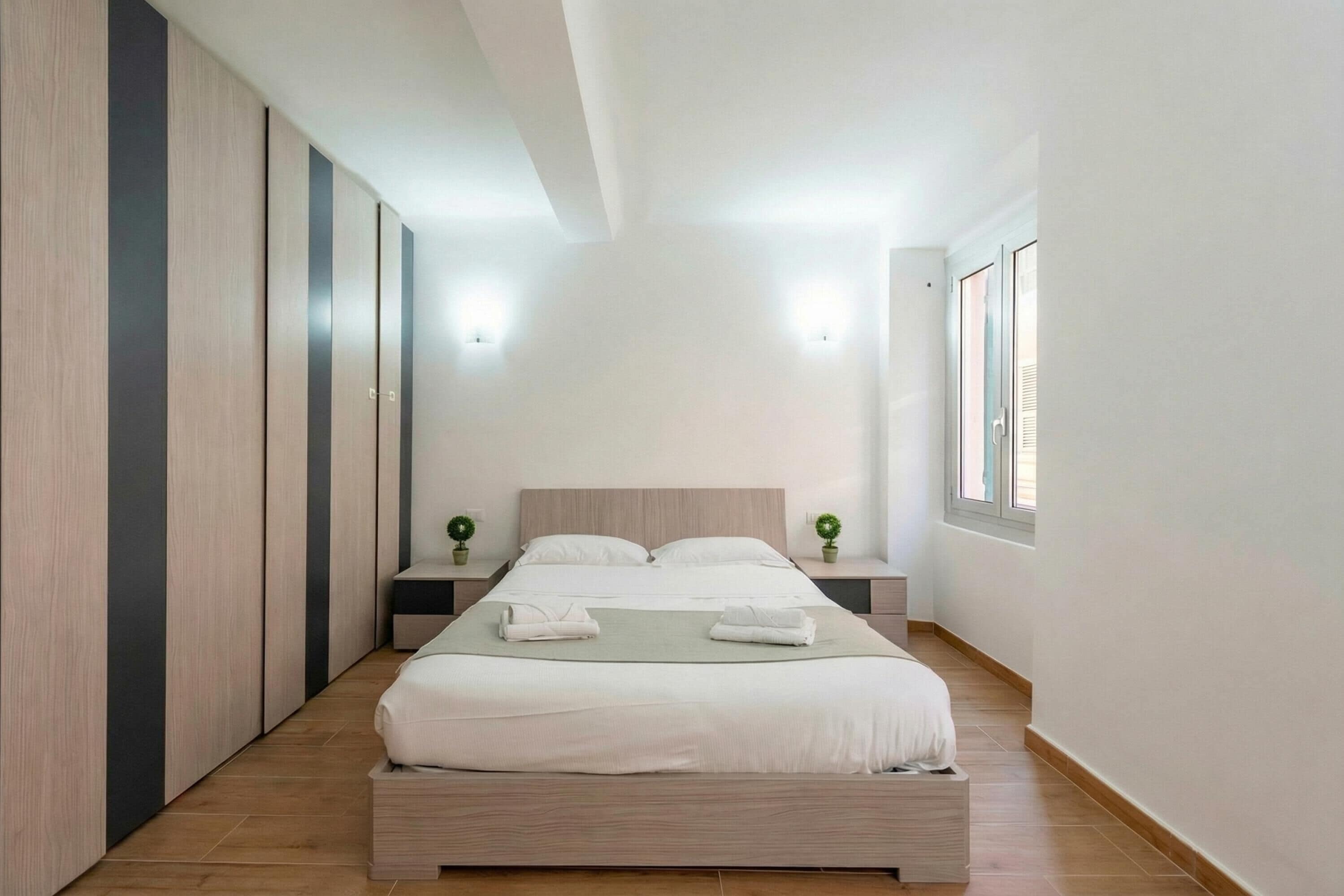 A modern bedroom with a large bed, bedside tables, a wardrobe, and a window.