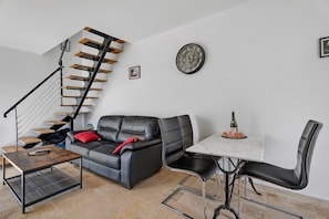 Una sala de estar moderna con un sofá de cuero negro, una mesa de comedor con sillas, una escalera con escalones de madera y un reloj de pared.