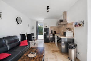 Una sala de estar moderna con un sofá de cuero negro, una mesa de centro de madera y una zona de cocina con microondas, estufa y fregadero.