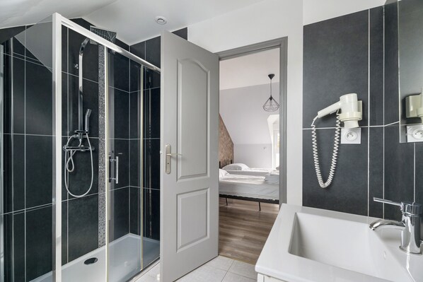 A modern bathroom with a glass shower enclosure, a white sink, and a hairdryer mounted on the wall.