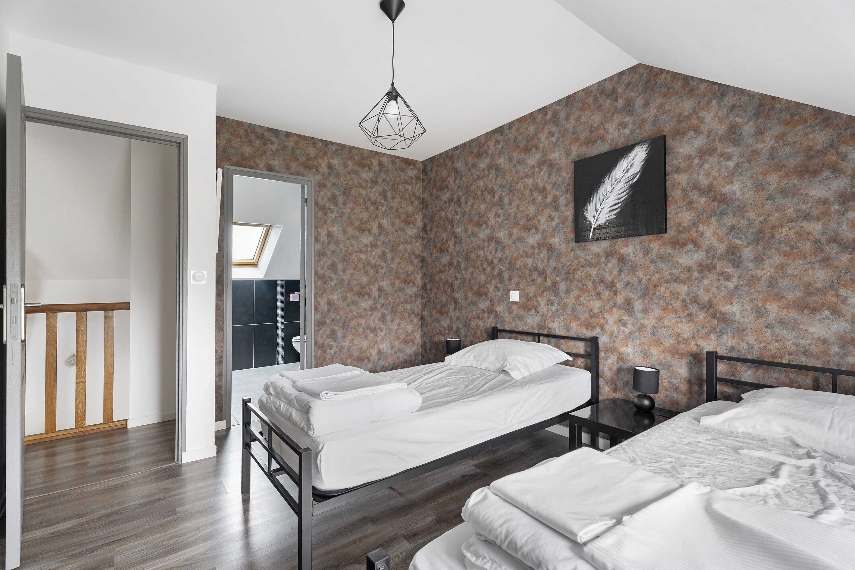 A bedroom with two beds, a skylight, a feather artwork, and a modern light fixture.