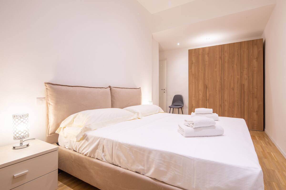 Une chambre à coucher moderne avec un lit, une table de chevet, une chaise et une armoire en bois.
