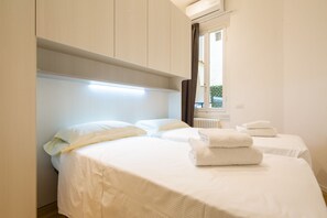 A hotel room with two beds, a headboard, a radiator, and a window with curtains. - Bargello Modern by Mmega (Florence)
