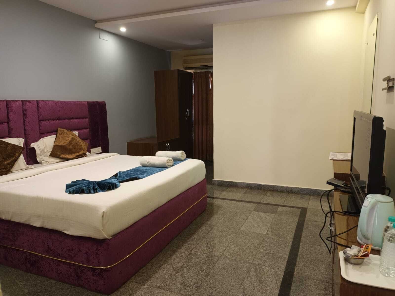 A hotel room with a bed, a desk with a computer, a television, and a bathroom door.
