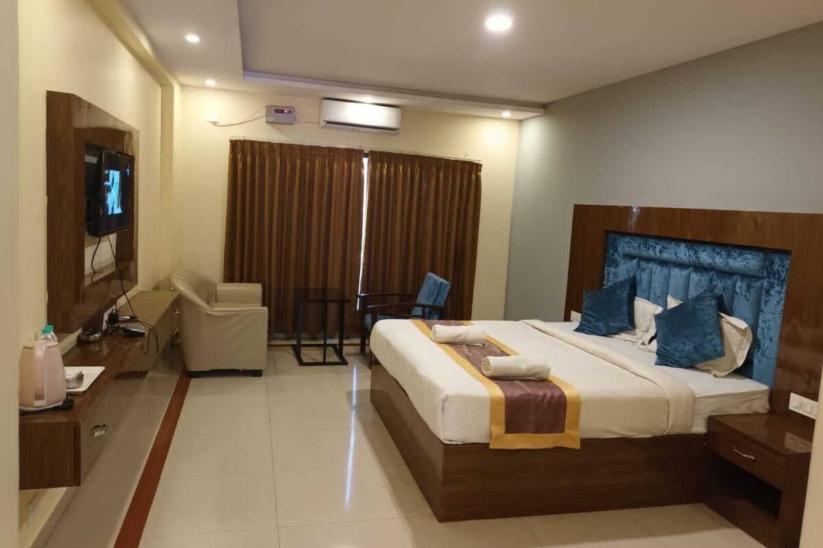 Habitación de hotel con cama, mesita de noche, silla, televisor, cortinas y aire acondicionado.