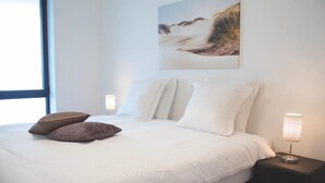 A neatly made bed with white bedding and two brown pillows, a bedside lamp, and a framed picture on the wall.
