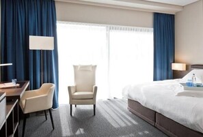 A hotel room with a bed, a desk, a chair, and a window with curtains. - Blue Woods Hotel (Deerlijk)