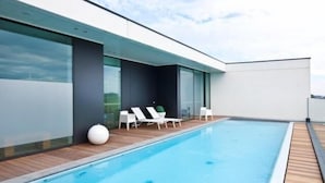 A modern outdoor swimming pool with wooden decking and white lounge chairs.