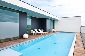 A modern outdoor swimming pool with wooden decking and white lounge chairs. - Blue Woods Hotel (Deerlijk)