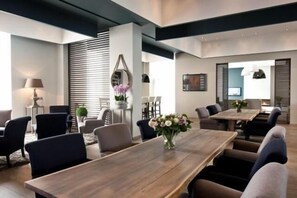 A modern dining area with a long wooden table, multiple chairs, and a vase of flowers. - Blue Woods Hotel (Deerlijk)