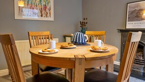 A round wooden dining table with chairs, a white mug, a blue and white patterned pitcher, and plates with cookies. - East Bank (Matlock)