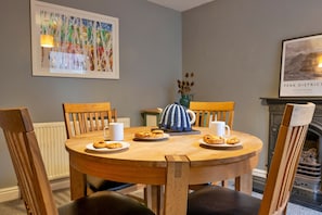 A round wooden dining table with chairs, a white mug, a blue and white patterned pitcher, and plates with cookies. - East Bank (Matlock)