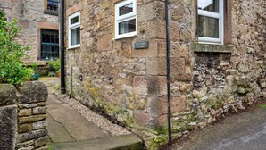 A stone cottage with a sign reading 'East Bank Cottage,' a small window, and a stone wall. - East Bank (Matlock)