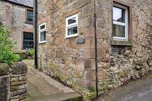 A stone cottage with a sign reading 'East Bank Cottage,' a small window, and a stone wall. - East Bank (Matlock)