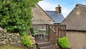 A stone building with a wooden deck, a stone wall, and a green chair. - East Bank (Matlock)