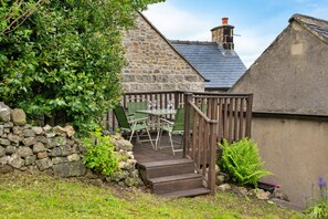 A stone building with a wooden deck, a stone wall, and a green chair. - East Bank (Matlock)