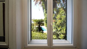 Ein Fenster mit Blick auf einen Swimmingpool, der von üppigem Grün umgeben ist.