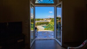 Eine offene Tür, die auf einen Balkon mit Blick auf ein Schwimmbad und viel Grün führt.