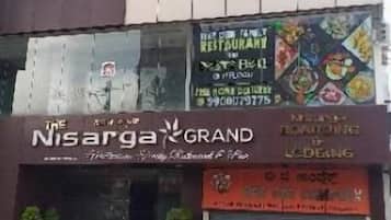 A building with multiple signs, including 'Nisarga GRAND' and 'BEG THE COMPLEX'.