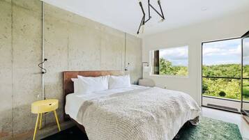 Une chambre avec un grand lit, une vue sur la verdure par la fenêtre et un mur en béton.