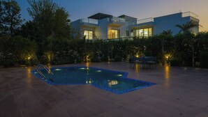 A modern house with a swimming pool, surrounded by trees and a patio area. - ELIVAAS Adhiva Retreat 5 BHK Farmhouse (Gurugram)