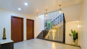 A spacious hallway with a marble floor, a staircase with a metal railing, and two wooden doors. - ELIVAAS Adhiva Retreat 5 BHK Farmhouse (Gurugram)