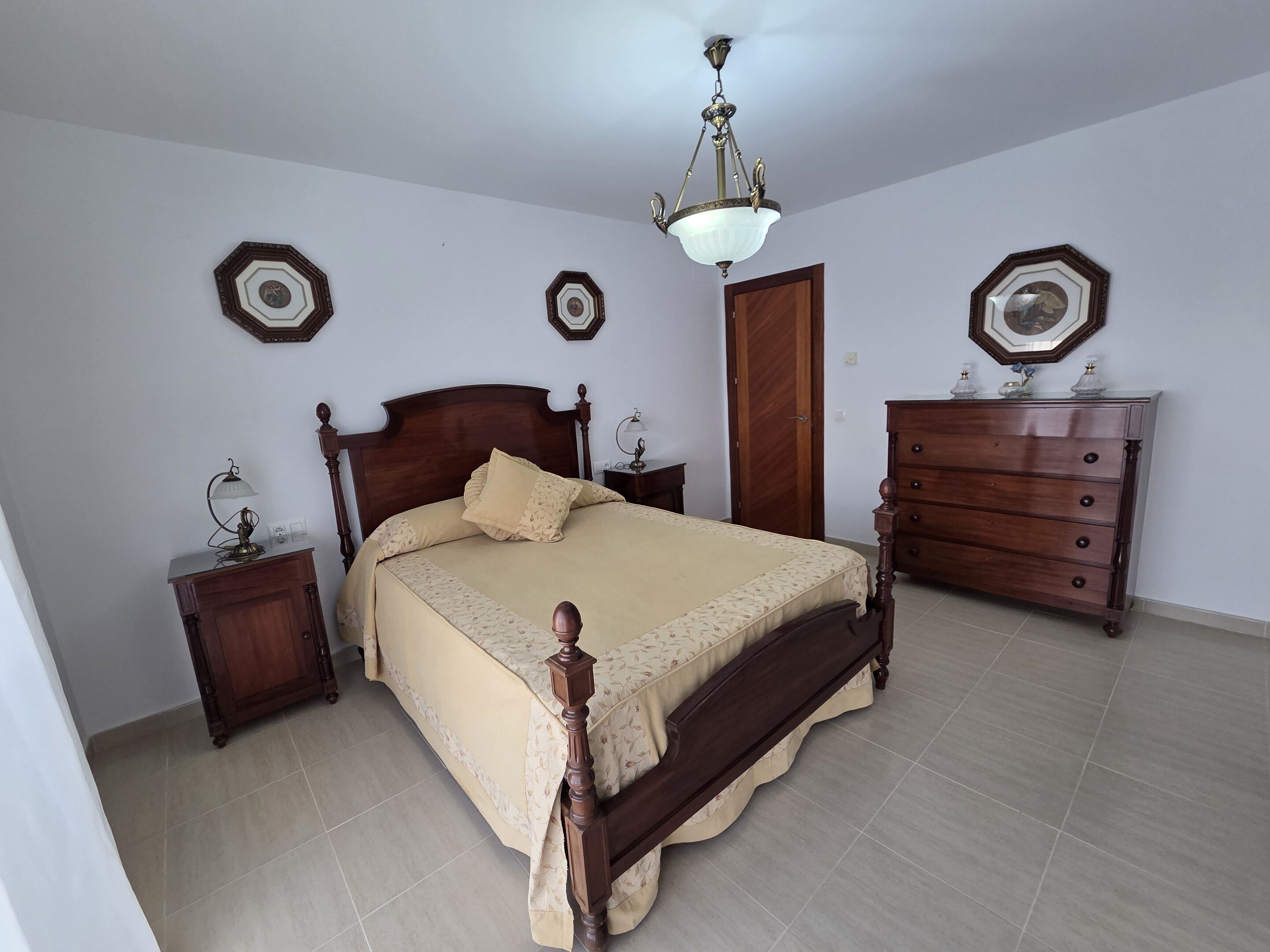 Ein Schlafzimmer mit einem hölzernen Bett, einem Schminktisch, einem Nachttisch und einer Chandelier.