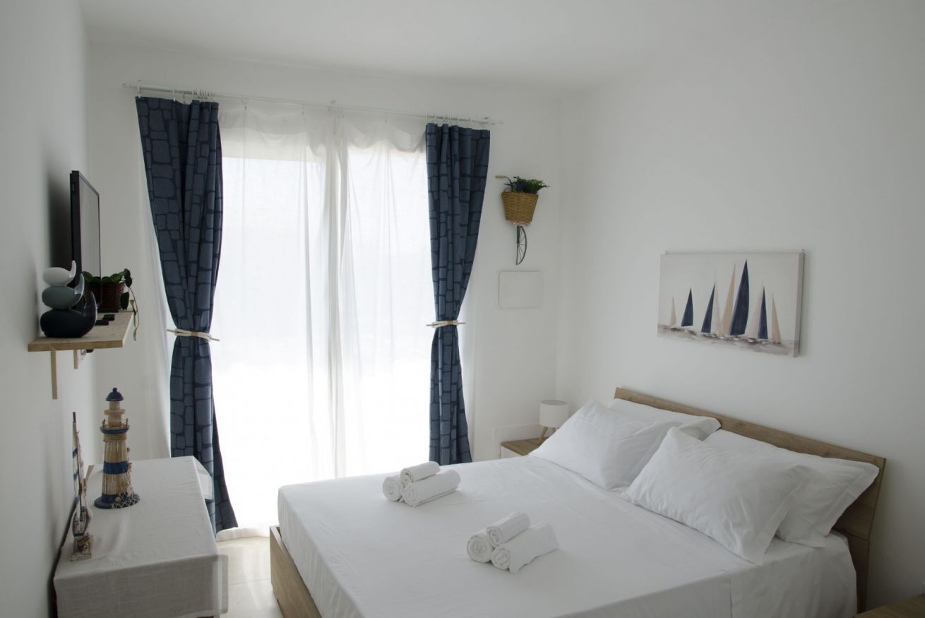 A hotel room with a bed, a nightstand, a lamp, a wall-mounted plant, and a painting.