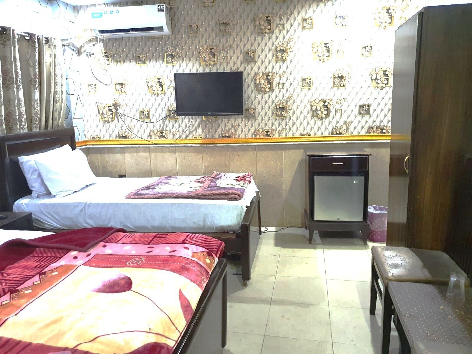 A hotel room with two beds, a television, a wardrobe, and a small table.