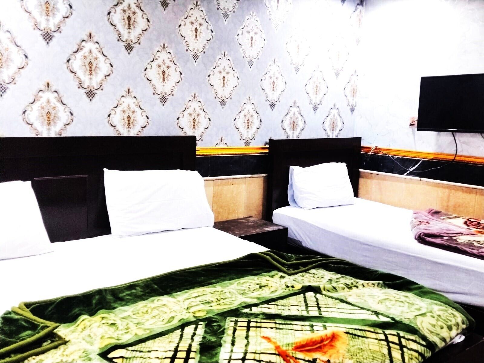 A hotel room with two beds, a television on the wall, and patterned wallpaper.