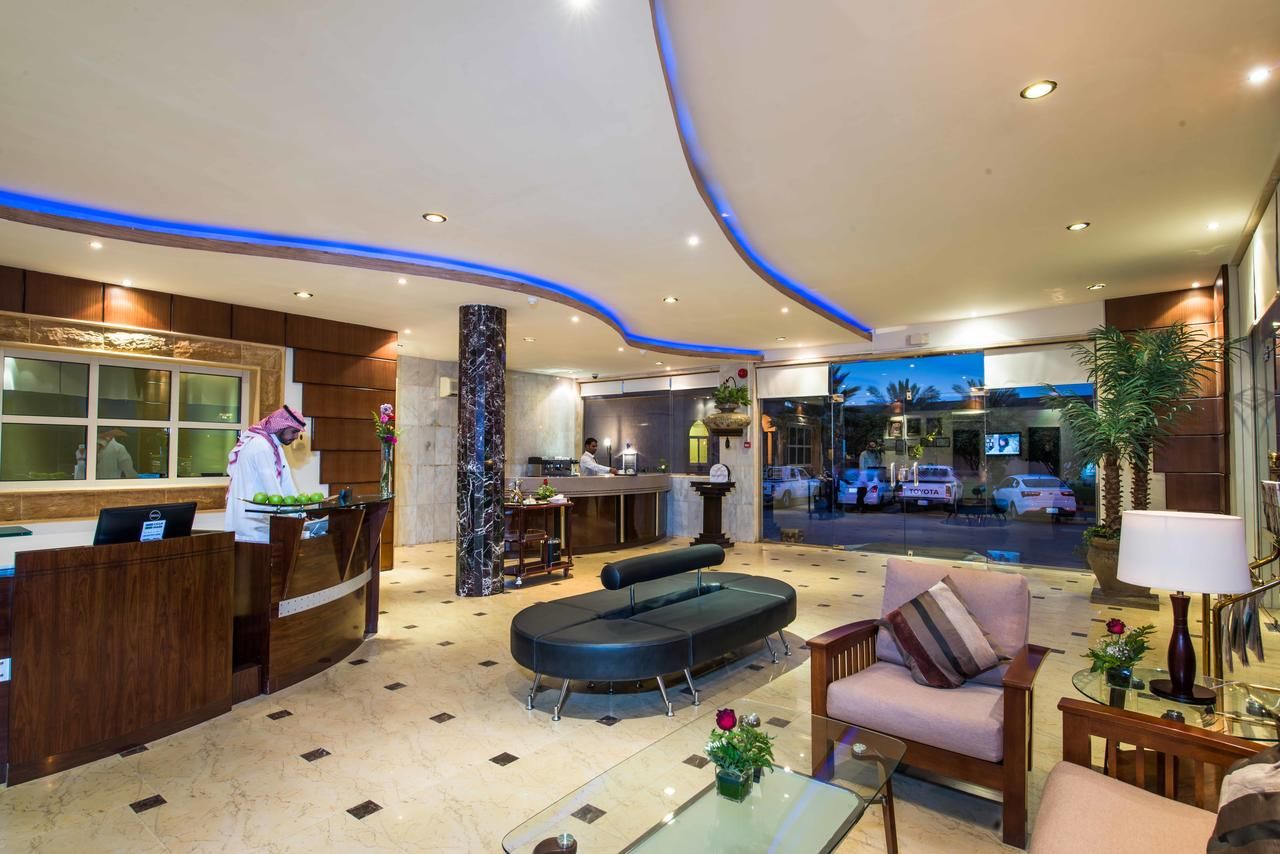 A hotel lobby with a reception desk, a bar, seating area, and a view of the street outside.