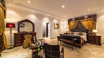 A spacious bedroom with a large bed, a sitting area with a sofa and chairs, a dining table with chairs, and a decorative mirror.