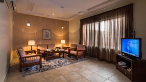 Habitación de hotel con televisión, dos sillones, una mesa de centro y un ventanal con cortinas.