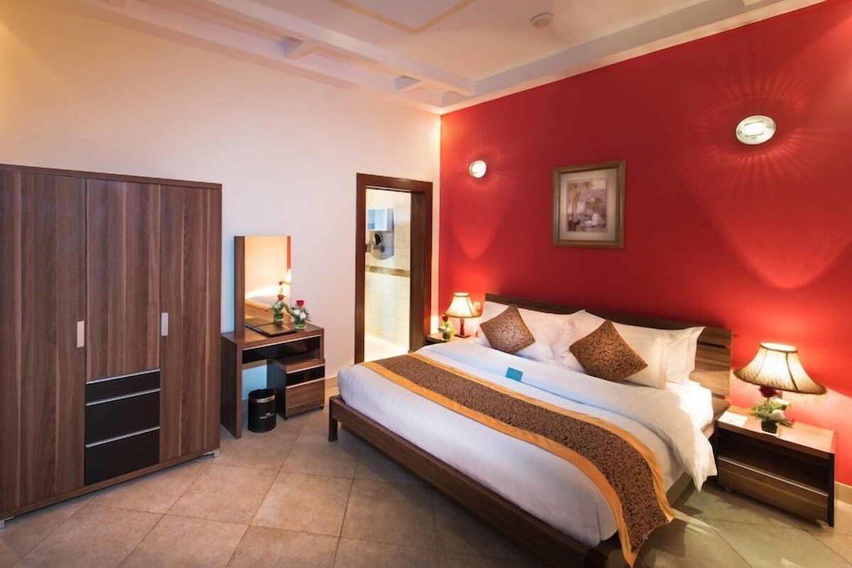 Una habitación de hotel con cama, armario, mesita de noche y espejo.