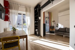 Una sala de estar moderna con comedor, sofá, estantería y un amplio ventanal con cortinas.