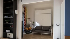 A modern living room with a sofa, a coffee table, a bookshelf, and a lamp. - Open Space Apartment near Lambrate Station (M2 and FS) & Politecnico (Milano)