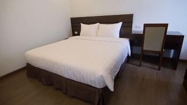 A neatly made bed with a wooden headboard, a bedside table, and a chair. - Poonsa Duy Tan Hotel & Serviced Apartment (Hanoi)