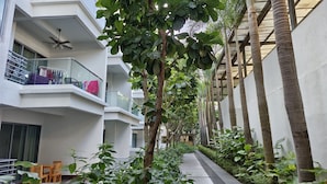 A narrow pathway flanked by lush greenery and tall palm trees, leading to a building with balconies and a ceiling fan. - Rasa Sayang at The Loft Imago (Kota Kinabalu)