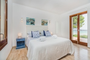 Ein Schlafzimmer mit Bett, Nachttisch, Fenster mit Blick und Kunstwerk an der Wand.