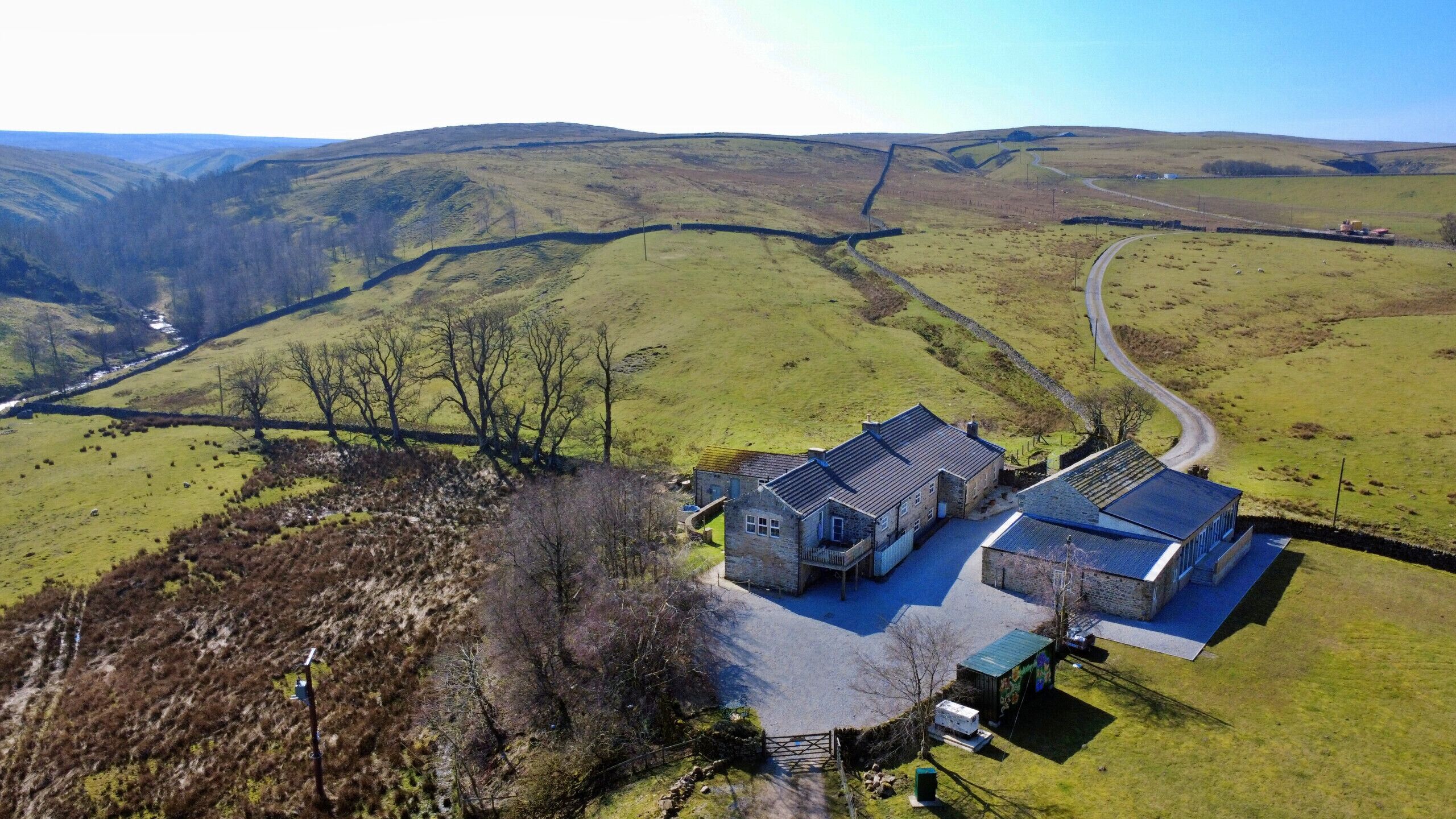 A rural property with stone buildings, a winding road, and rolling hills in the background.